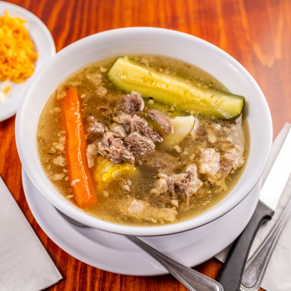 Hearty Mexican beef soup with carrots, corn, and zucchini, served with a side of rice.