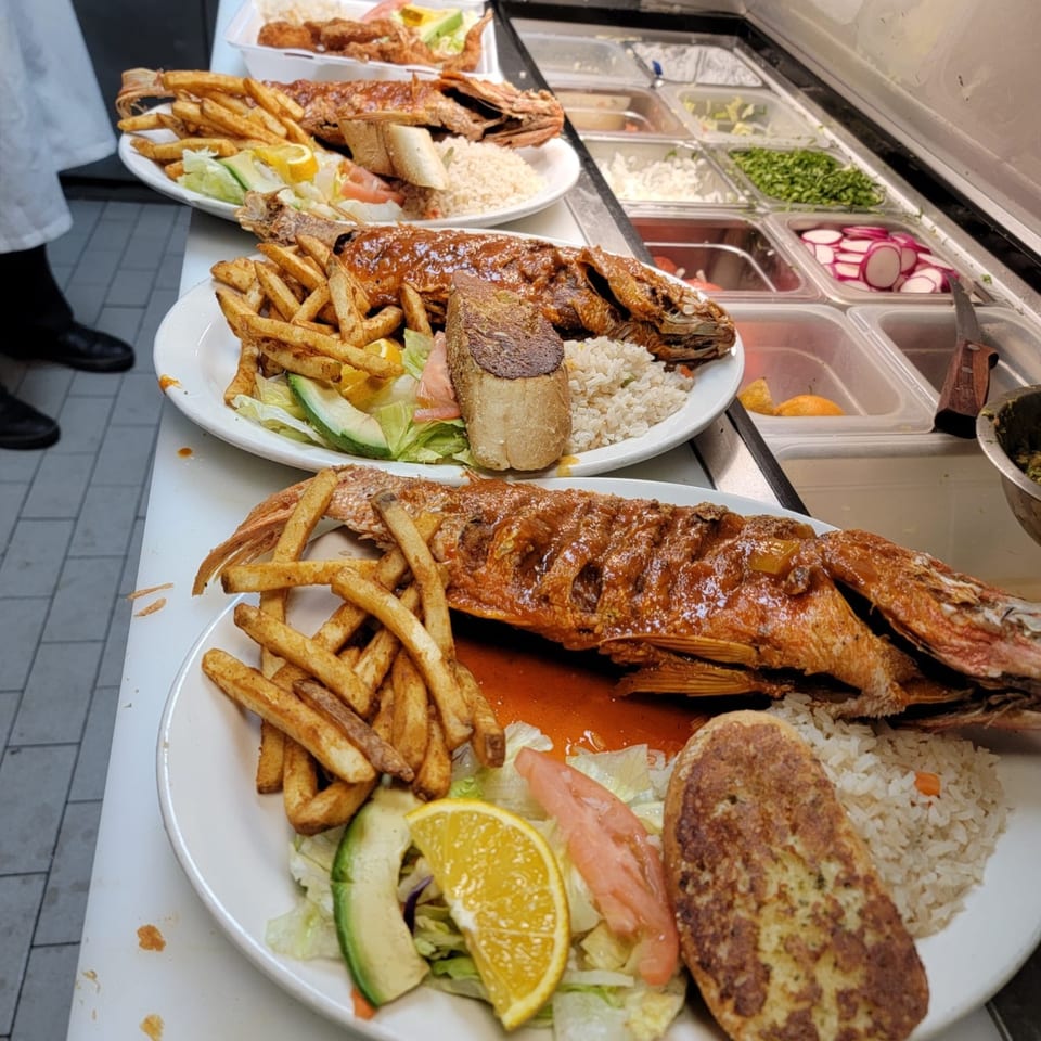 Three plates of whole fried fish with fries, rice, and salad, on a counter next to a salad bar.