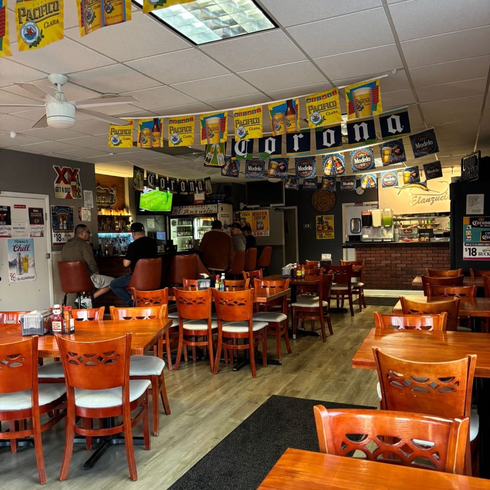 Interior of El Anzuelo Restaurant with wooden tables, chairs, a bar area, and Mexican beer banners.