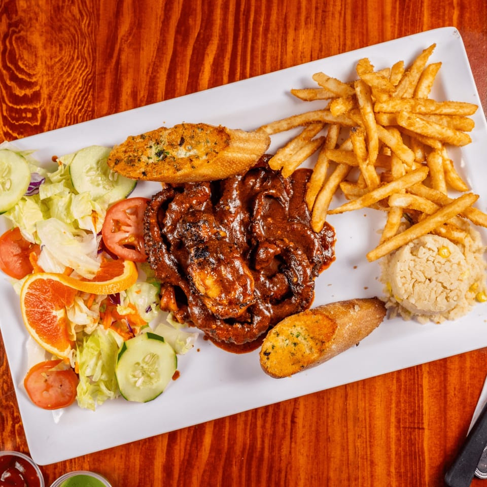 A Mexican dish with saucy meat, fries, rice, garlic bread, and a fresh salad with orange slices.