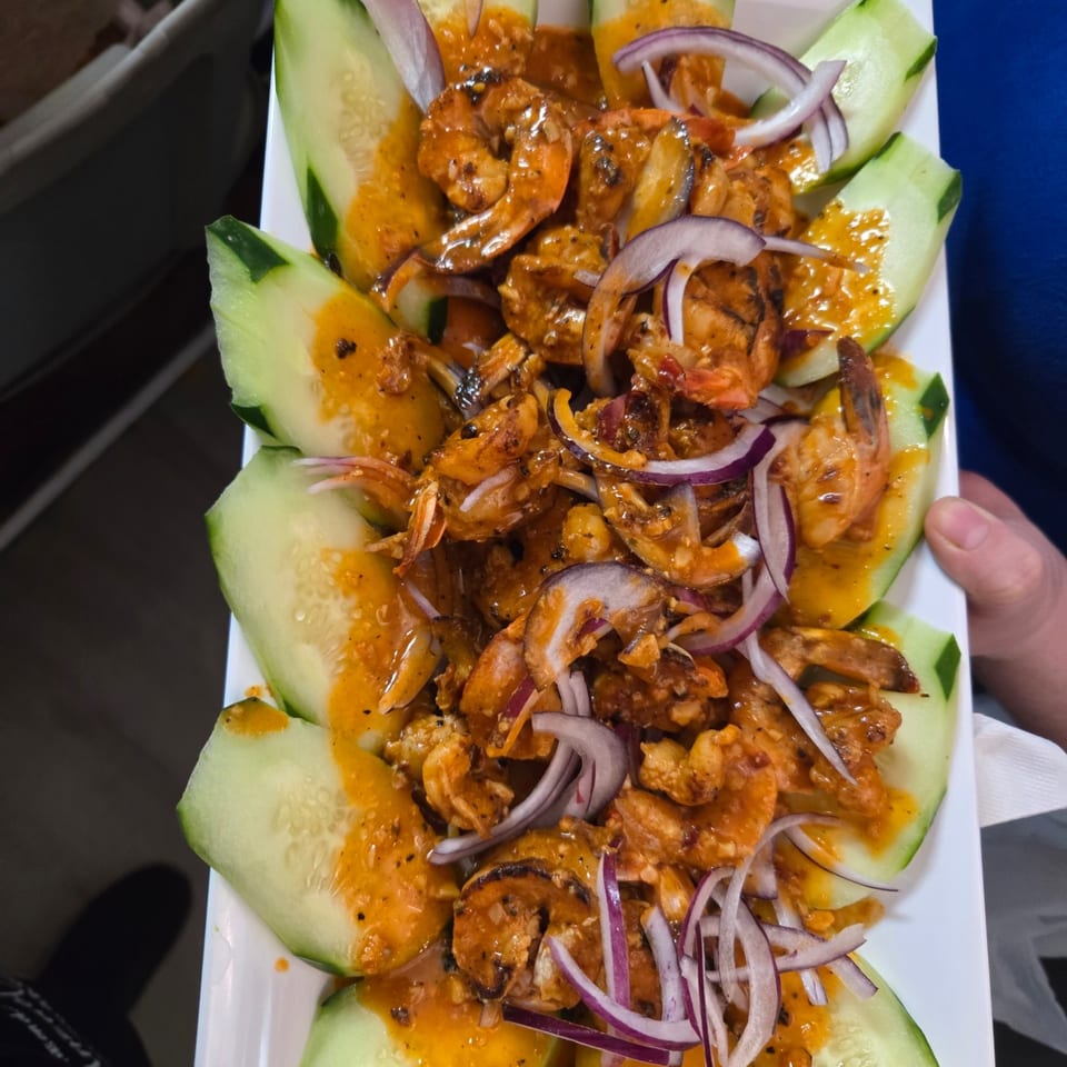 Mexican shrimp dish with red sauce, red onions, and cucumber slices on a white plate.