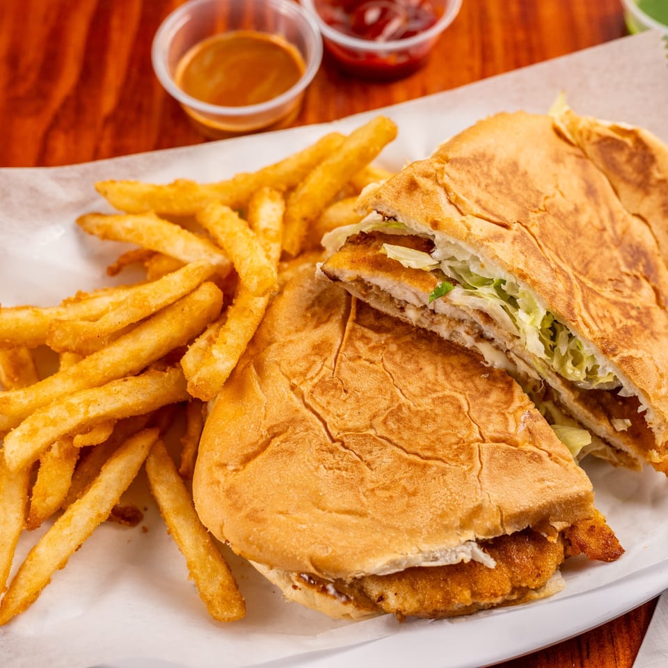 Mexican torta sandwich with fried chicken and shredded lettuce, served with golden french fries.