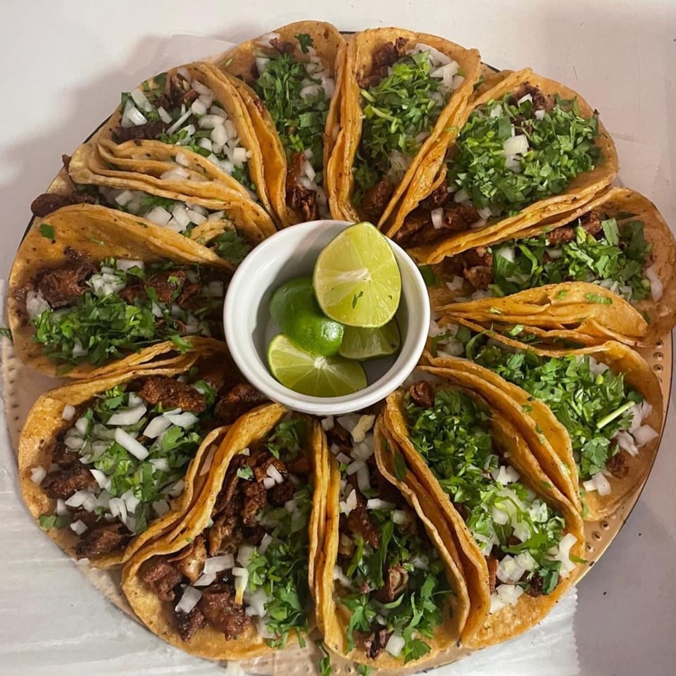 A platter of El Anzuelo Restaurant's Mexican tacos, garnished with cilantro, onions, and a side of lime wedges.