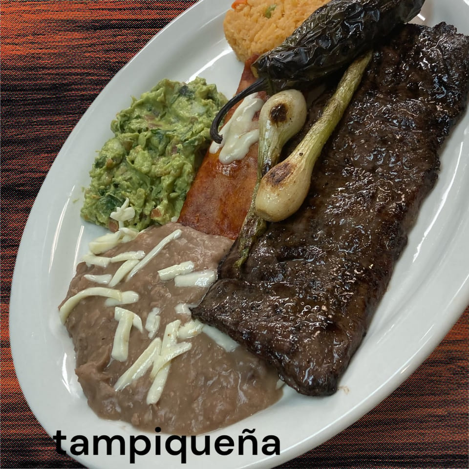 El Anzuelo's Tampiqueña: grilled steak, refried beans, guacamole, rice, and roasted peppers on a white plate.