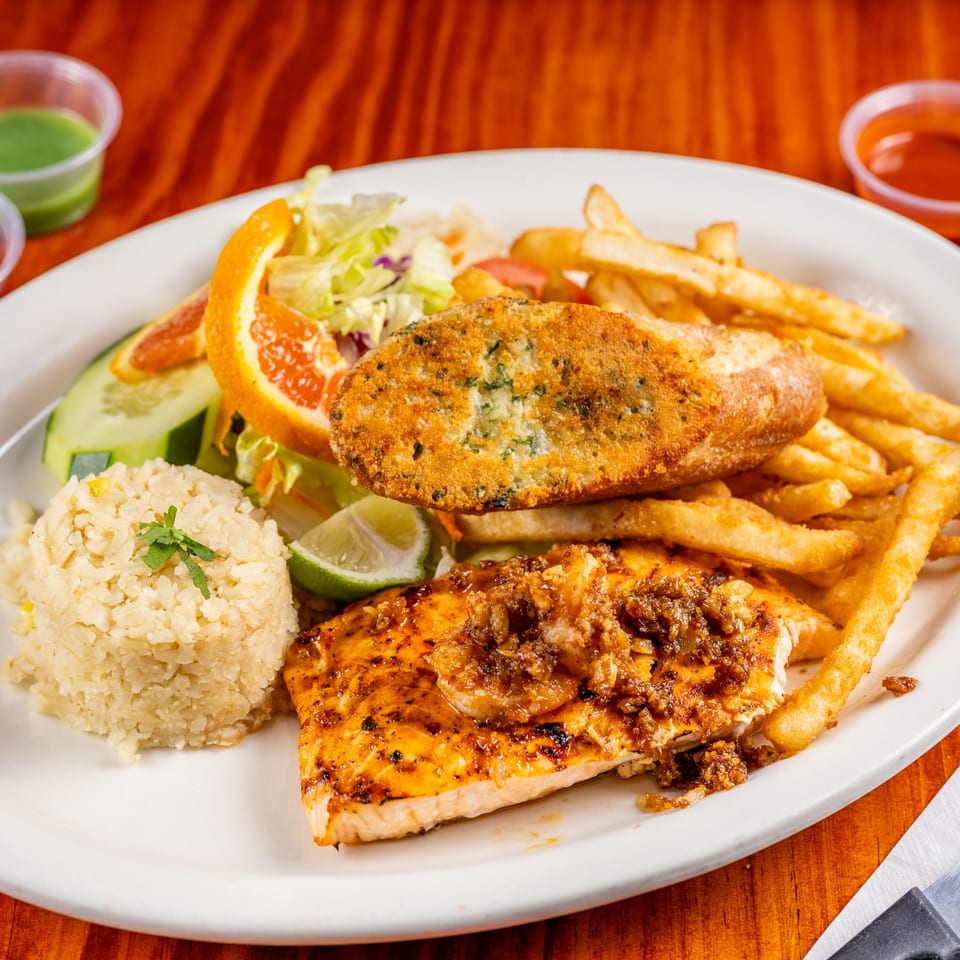 Mexican grilled salmon and breaded fish fillet with rice, fries, salad, and orange slices.