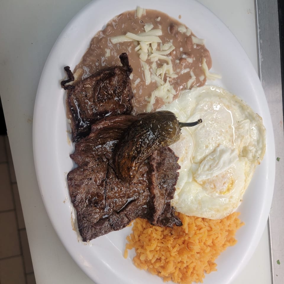 Mexican breakfast plate with grilled steak, fried eggs, refried beans with cheese, and orange rice.