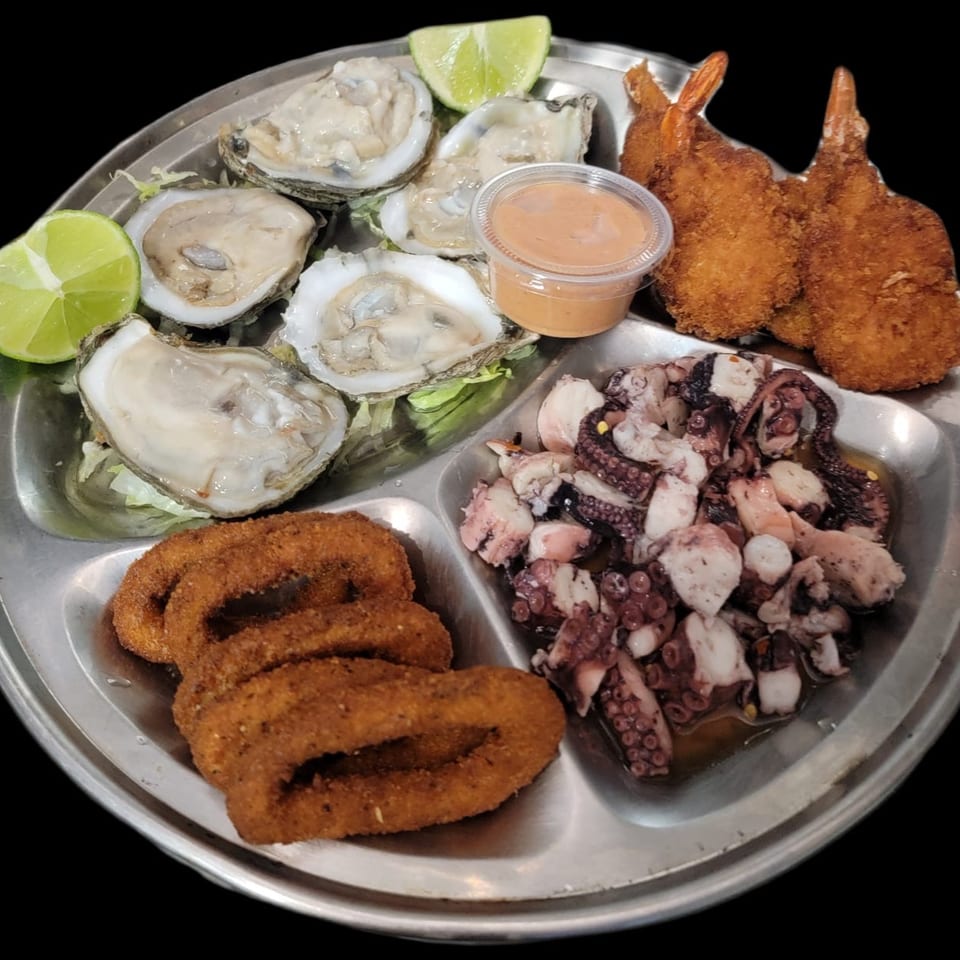 A metal platter with oysters, fried shrimp, calamari, and octopus ceviche, garnished with lime.