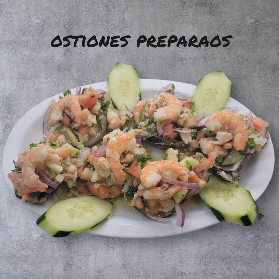 Mexican prepared oysters topped with shrimp, diced tomatoes, onions, and cilantro, garnished with cucumber slices.